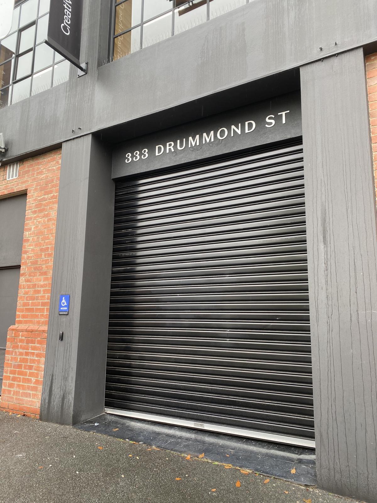 The 333 Drummond St entrance with its black roller shutter down, as it looks outside business hours.