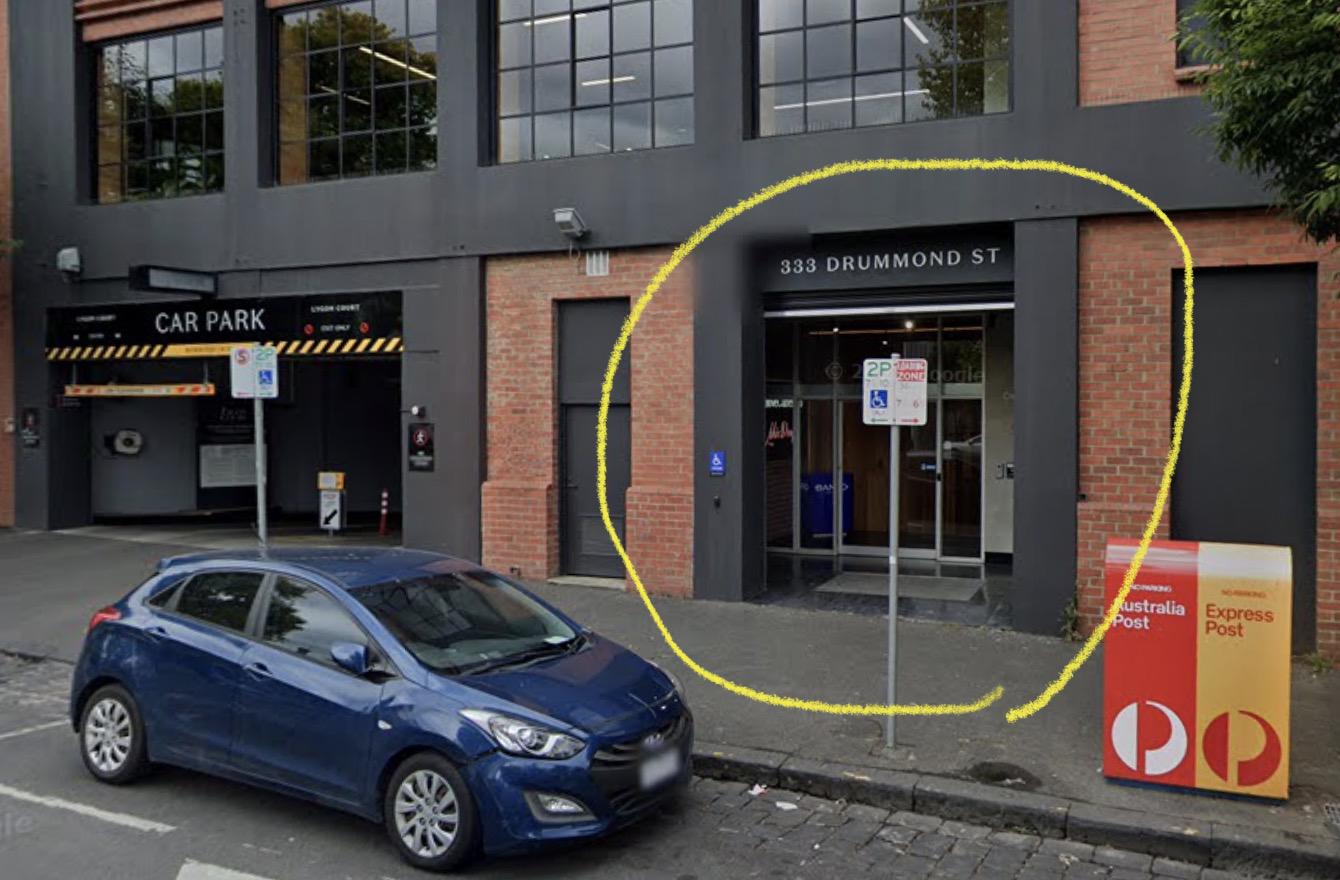 Street view of 333 Drummond St, with the entrance circled in yellow, the Lygon Court car park to its left and an Australia Post box to its right.